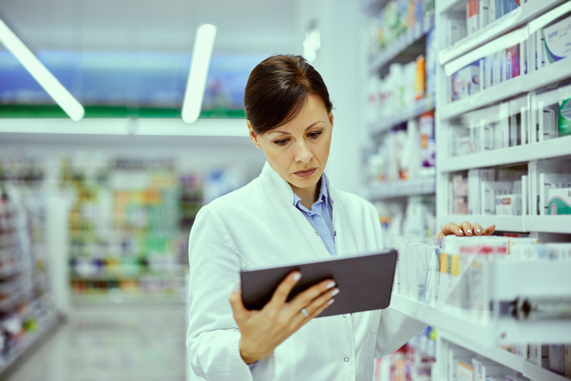 Una farmacéutica trabaja sobre una tableta y revisa los productos en los estantes.